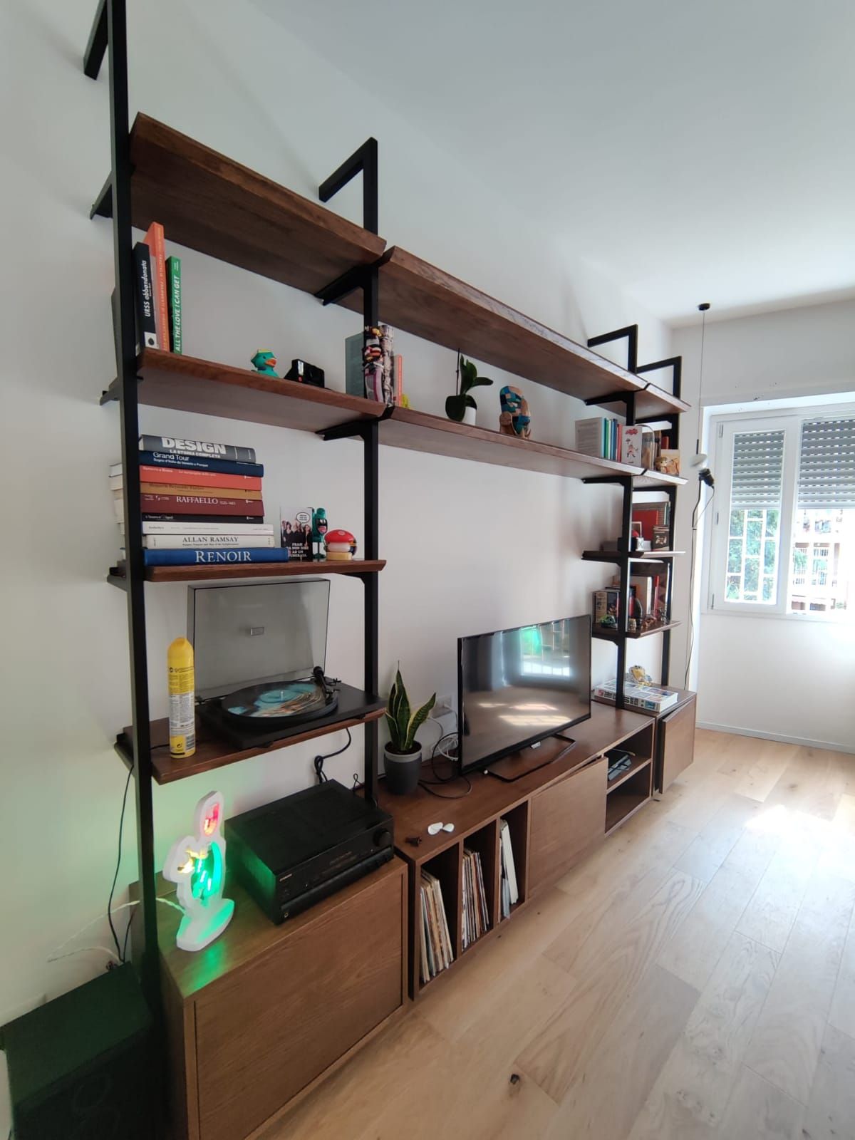 Libreria in legno con TV, libri e decorazioni contro una parete bianca e un pavimento in legno chiaro.