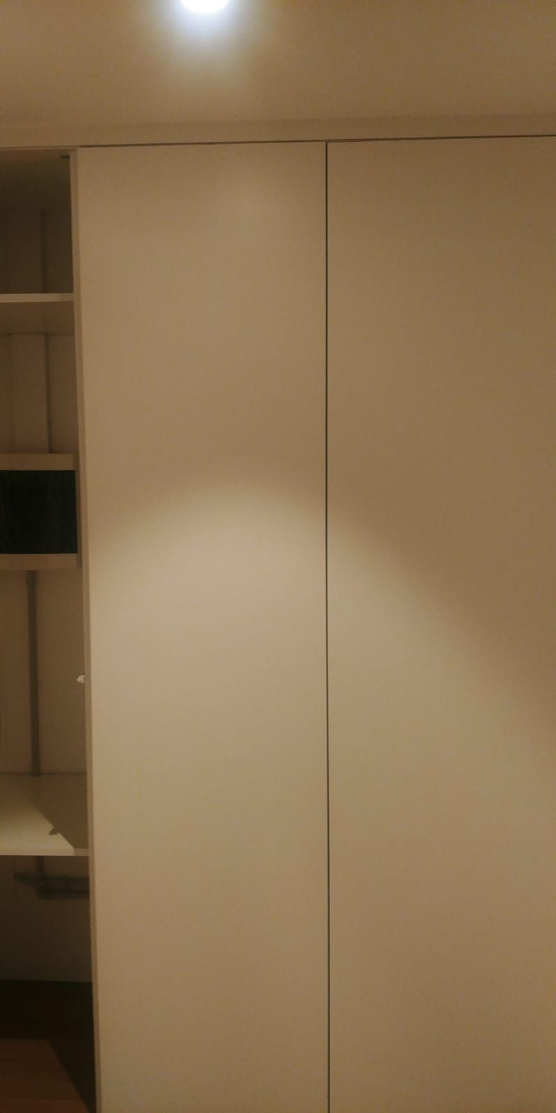 Ante dell'armadio bianche e scaffalature con un'unica lampada.