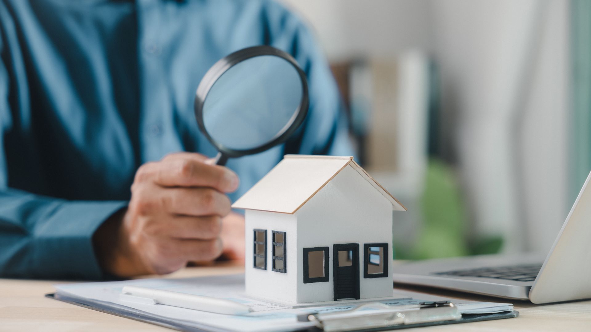 Real estate agent using magnifying glass to inspect miniature house model for property appraisal.