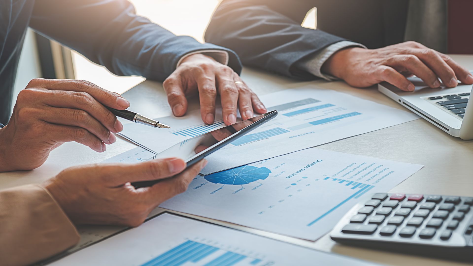 Hands reviewing financial charts and calculations with a laptop and calculator on a desk