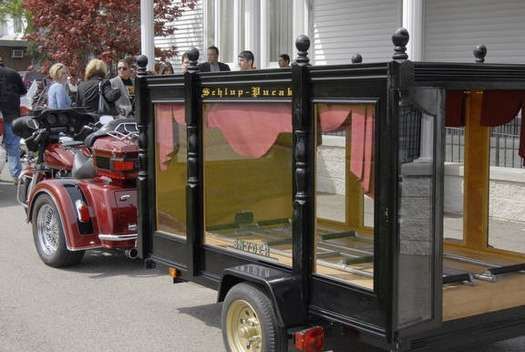 A motorcycle is pulling a trailer with a coffin on it.