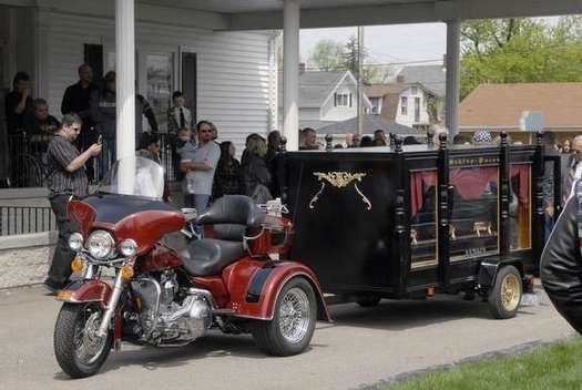 A red motorcycle is pulling a black hearse