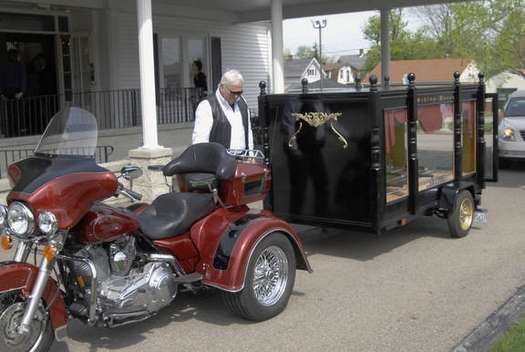 A man is standing next to a red motorcycle and a black trailer.