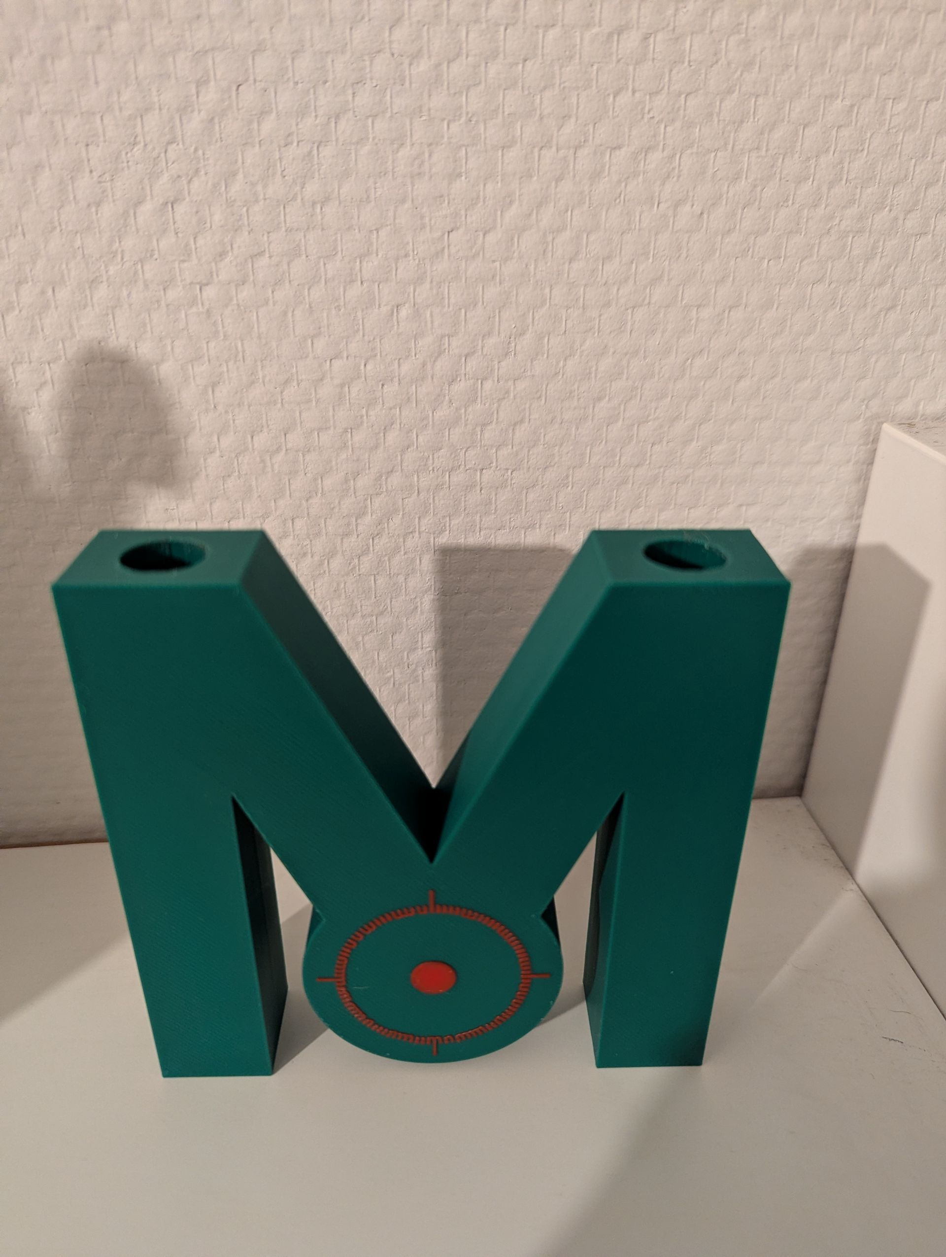 Rig-3d Een turquoise M-vormig object met een cirkelvormig ontwerp in het midden en gaten aan de bovenkant.