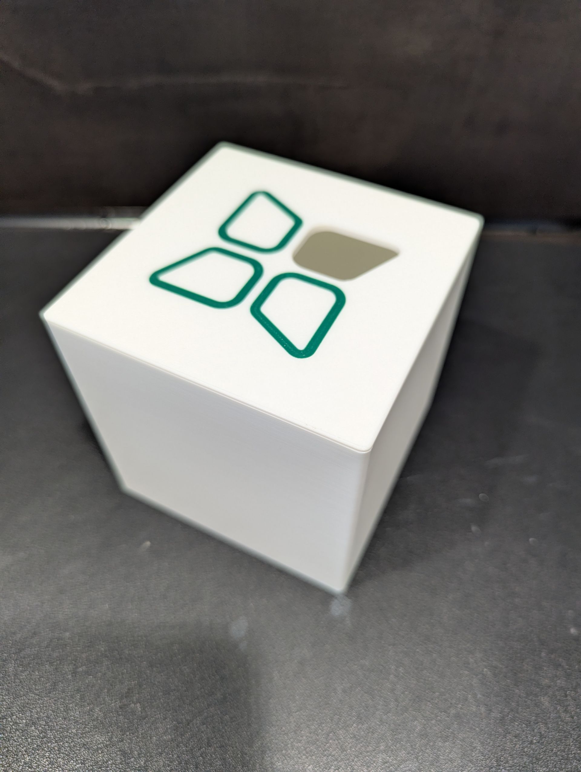 Witte kubus met een groen en grijs geometrisch logo op een donkere achtergrond.