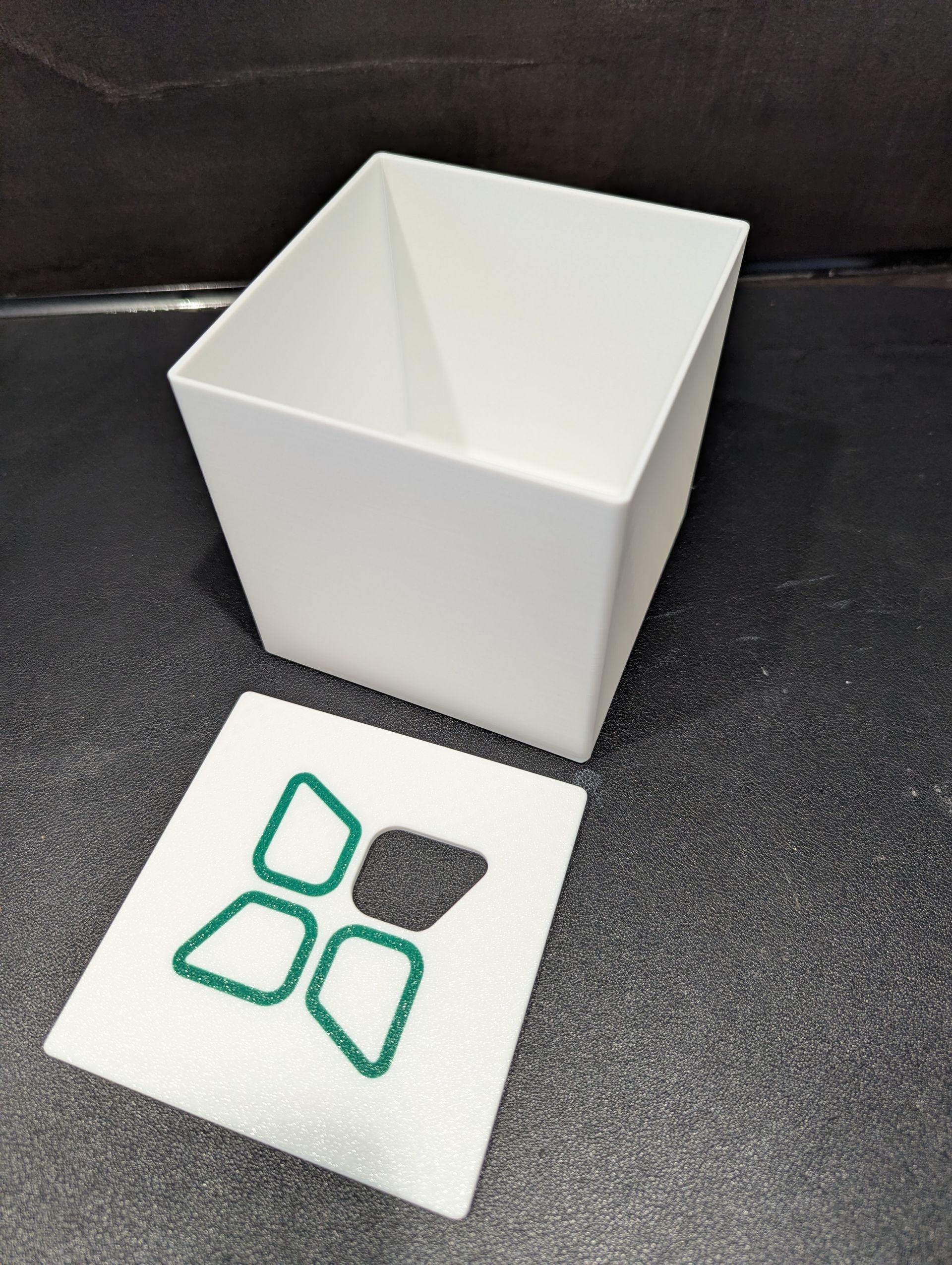 Witte kubus met een groen en grijs geometrisch logo op een donkere achtergrond.