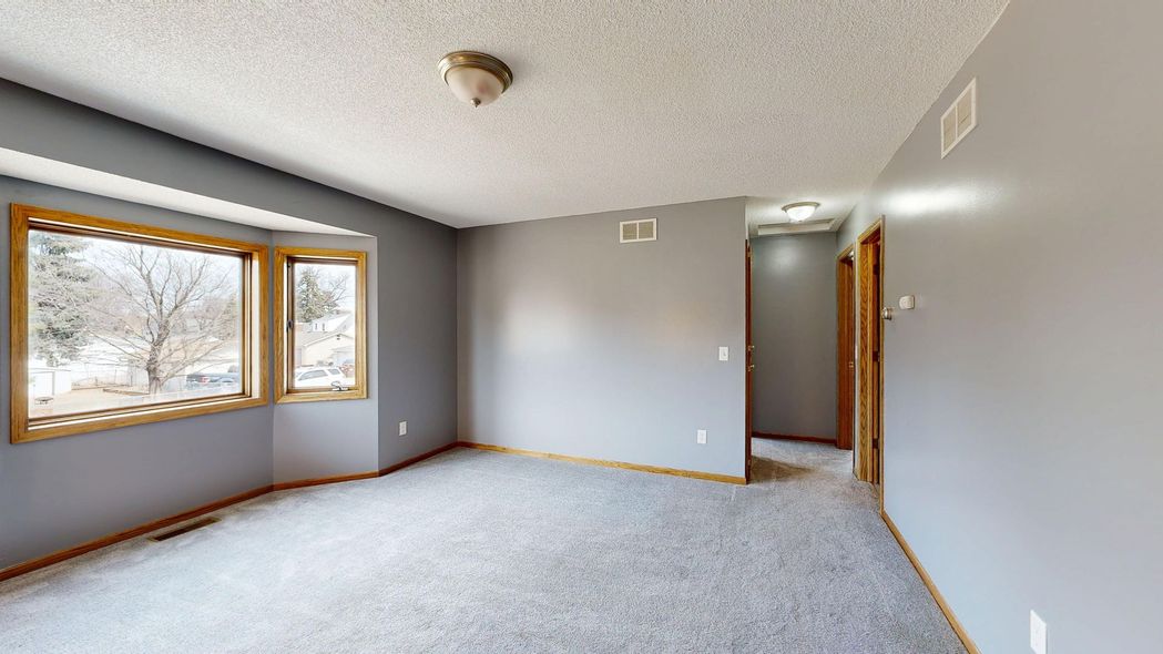 Empty gray bedroom with carpet, two windows, and an open doorway.