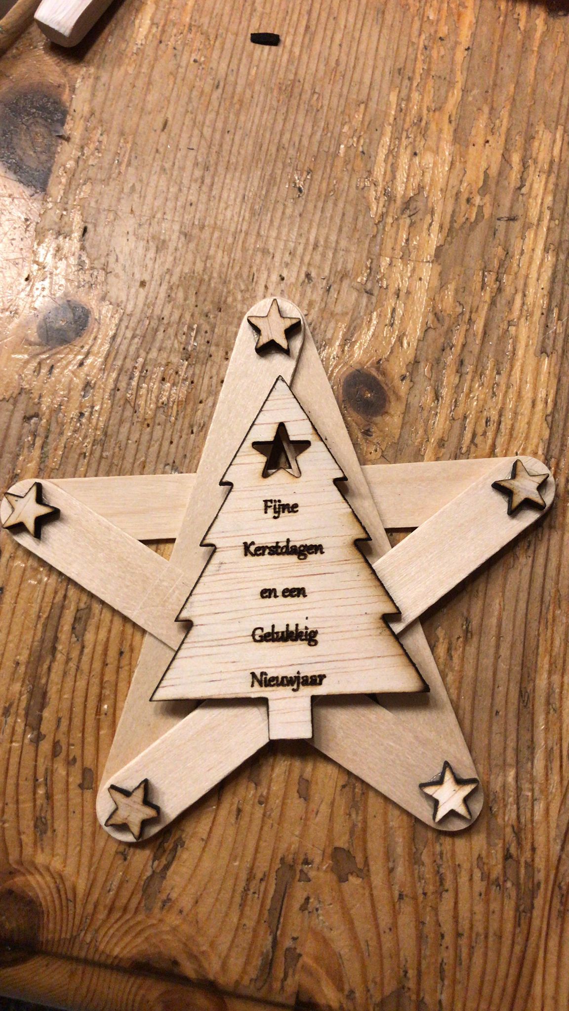Houten sterornament met een lasergesneden kerstboom in het midden en sterretjes op de punten.