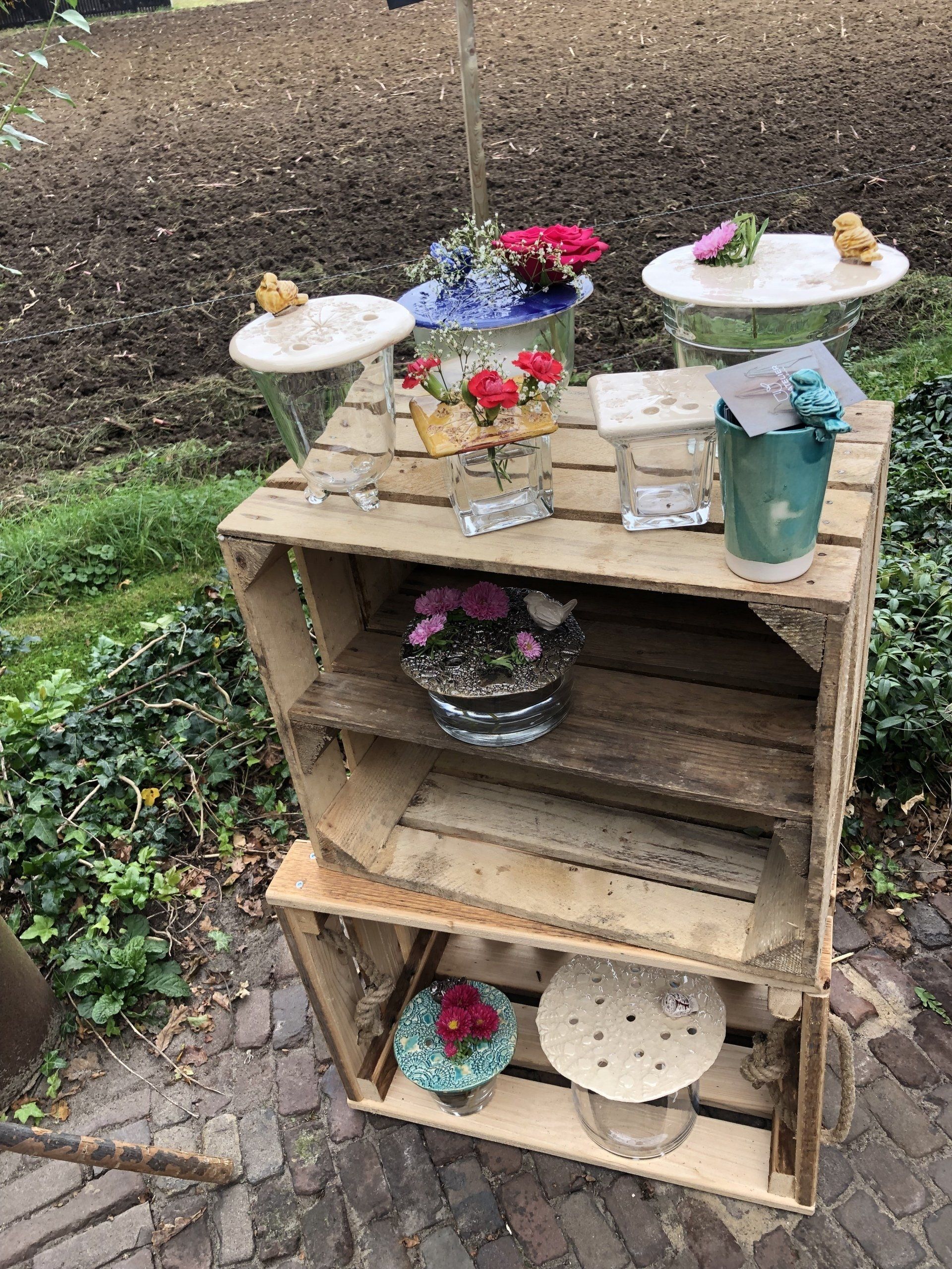 In houten kratten worden bloemen en kleine versieringen buiten tentoongesteld.