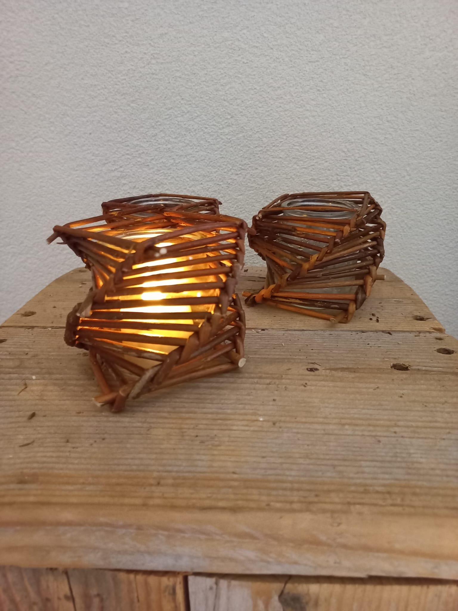 Twee spiraalvormige houten lantaarns op een rustieke houten ondergrond, die warm licht verspreiden tegen een neutrale muur.