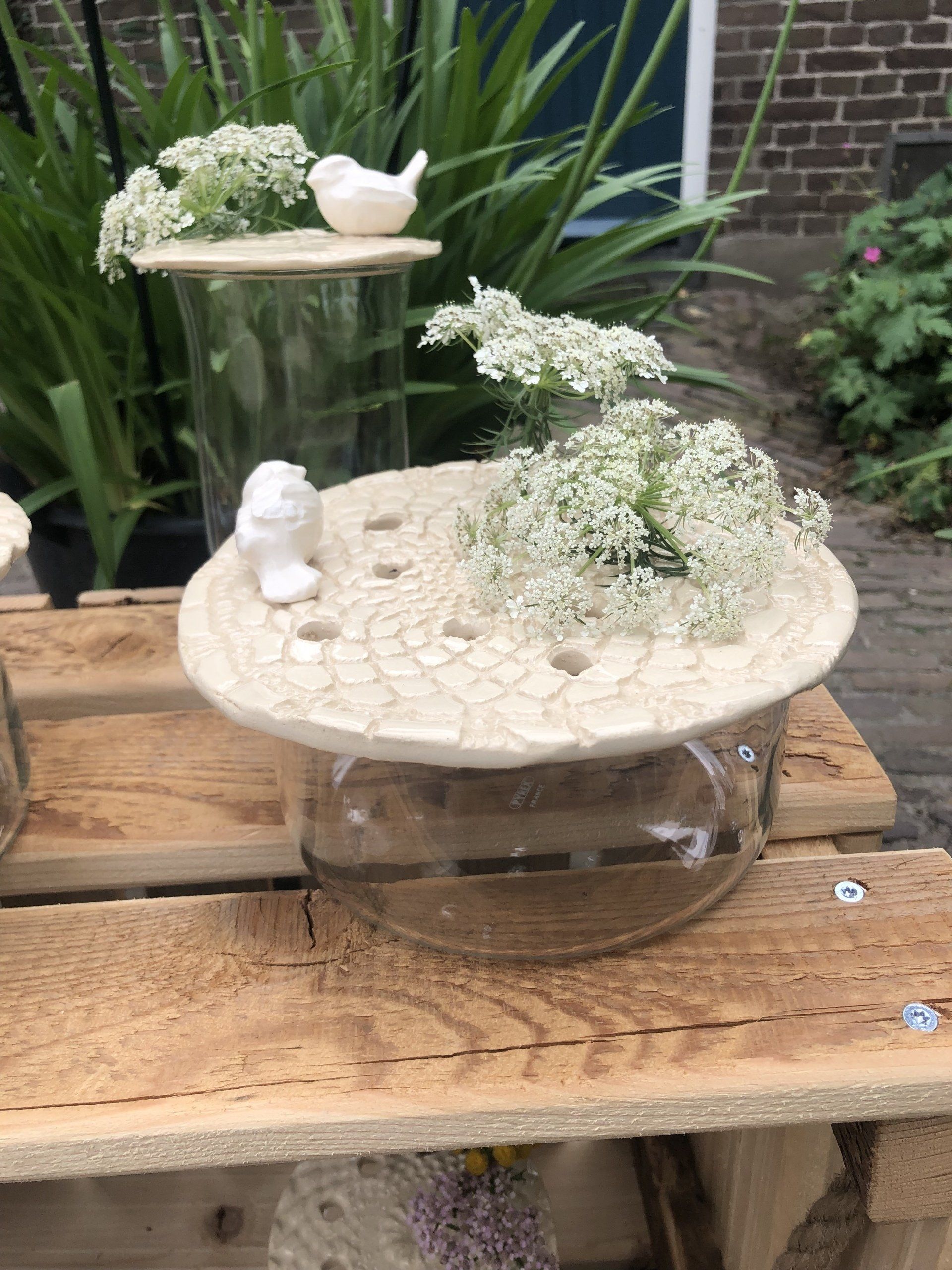 Twee glazen vazen met bloemstukken en kleine witte vogelfiguurtjes op een houten ondergrond.
