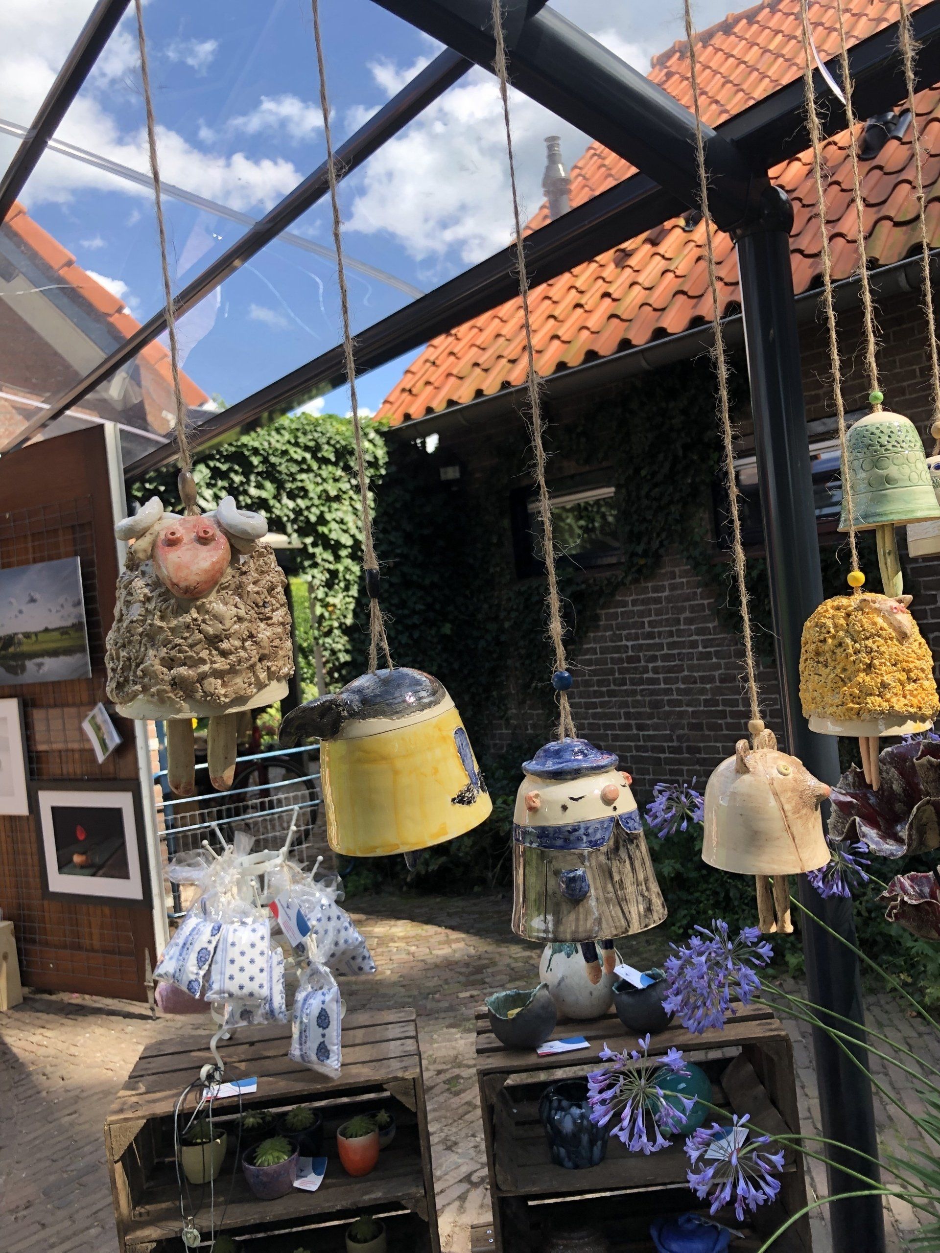 Keramische windgong die buiten hangt; in diverse vormen, kleuren en texturen, met houten kratten en groen.