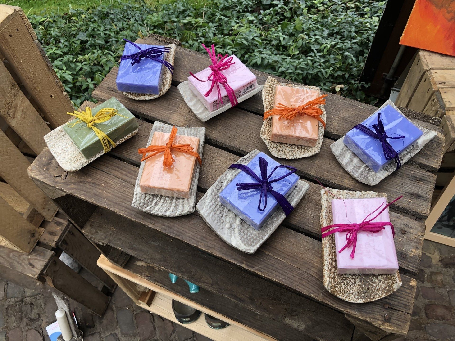 Negen kleurrijk verpakte zeepjes op een rustieke houten display, elk met een lintje eromheen.