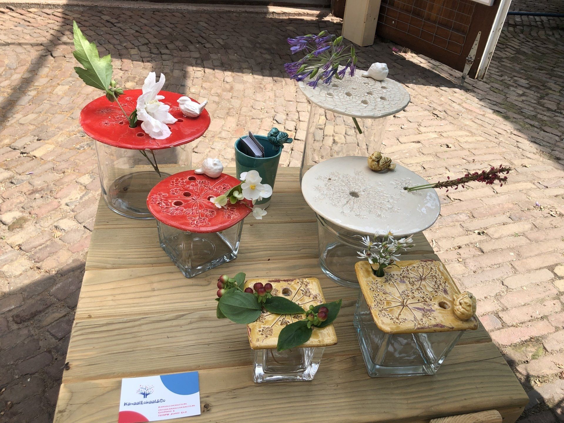 Bloemstukken op glazen standaards, tentoongesteld op een houten tafel. Rode, witte en beige decoratieve elementen met bloemen.