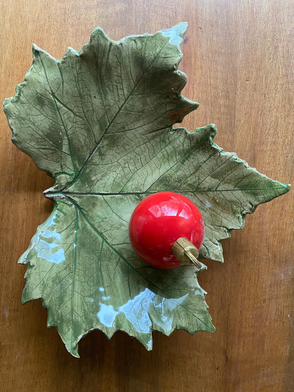 Rood ornament op een groene, bladvormige keramische schaal, geplaatst op een houten ondergrond.