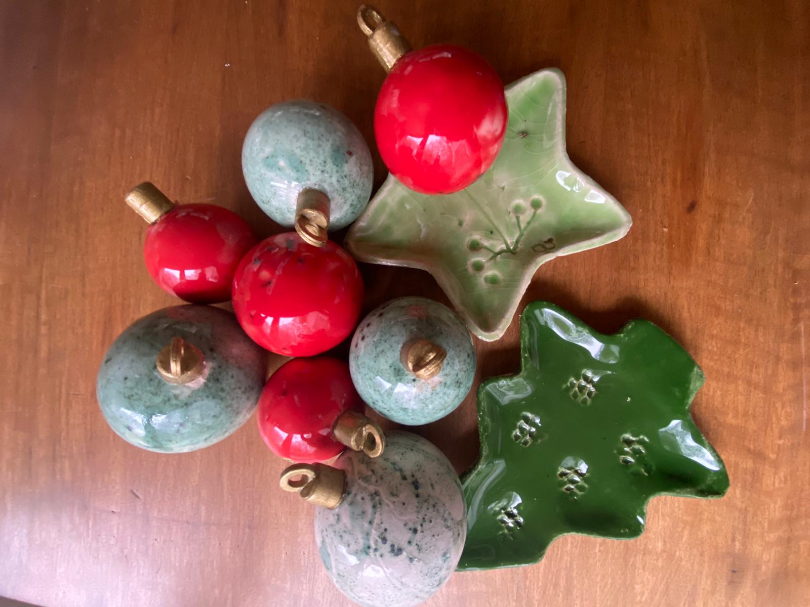 Een verzameling keramische kerstversieringen, waaronder rode ballen, gespikkelde turquoise ballen en schalen in de vorm van sterren en bomen.