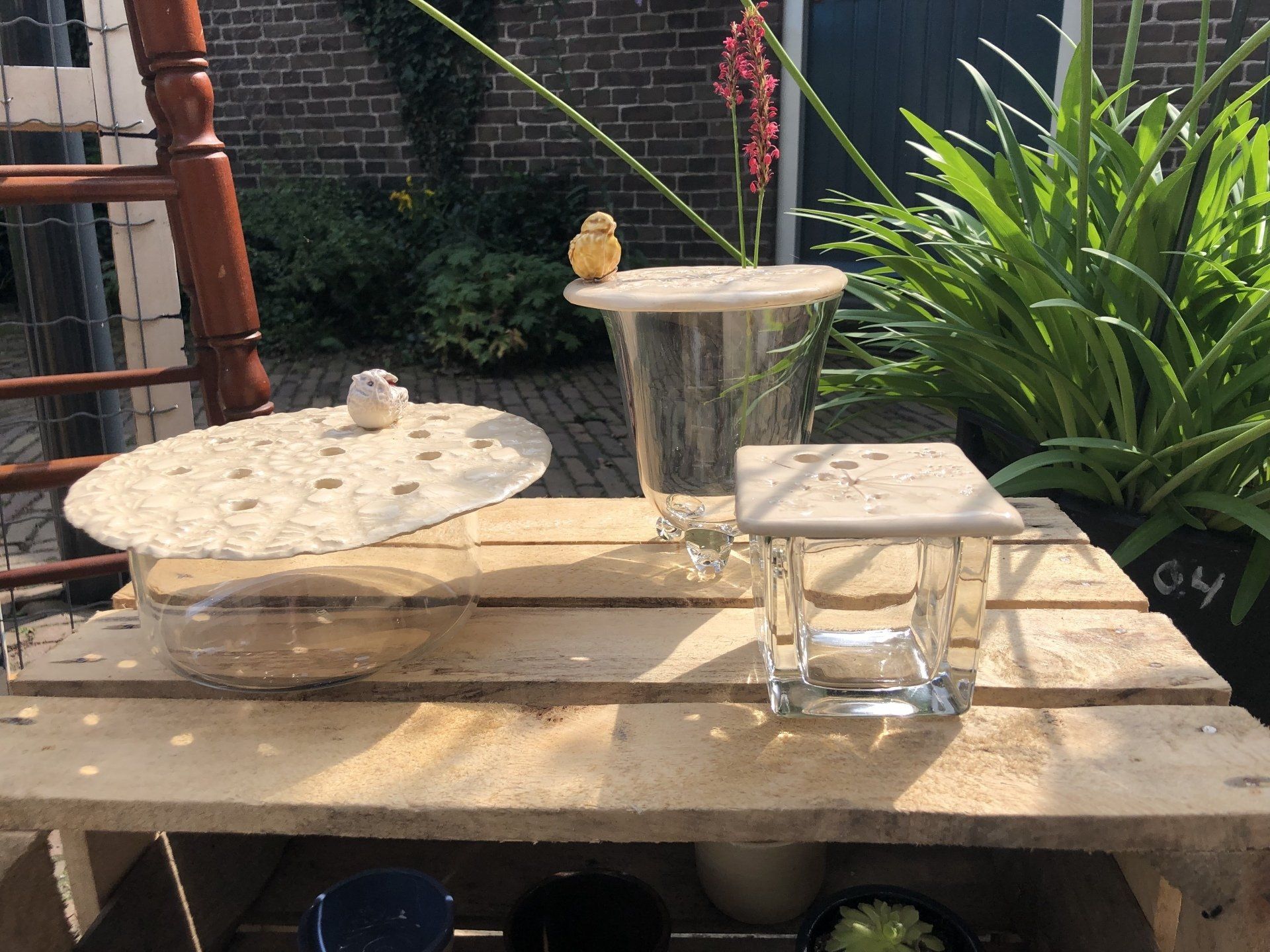 Houten tafel met glazen vazen en een klein vogelbeeldje ernaast.