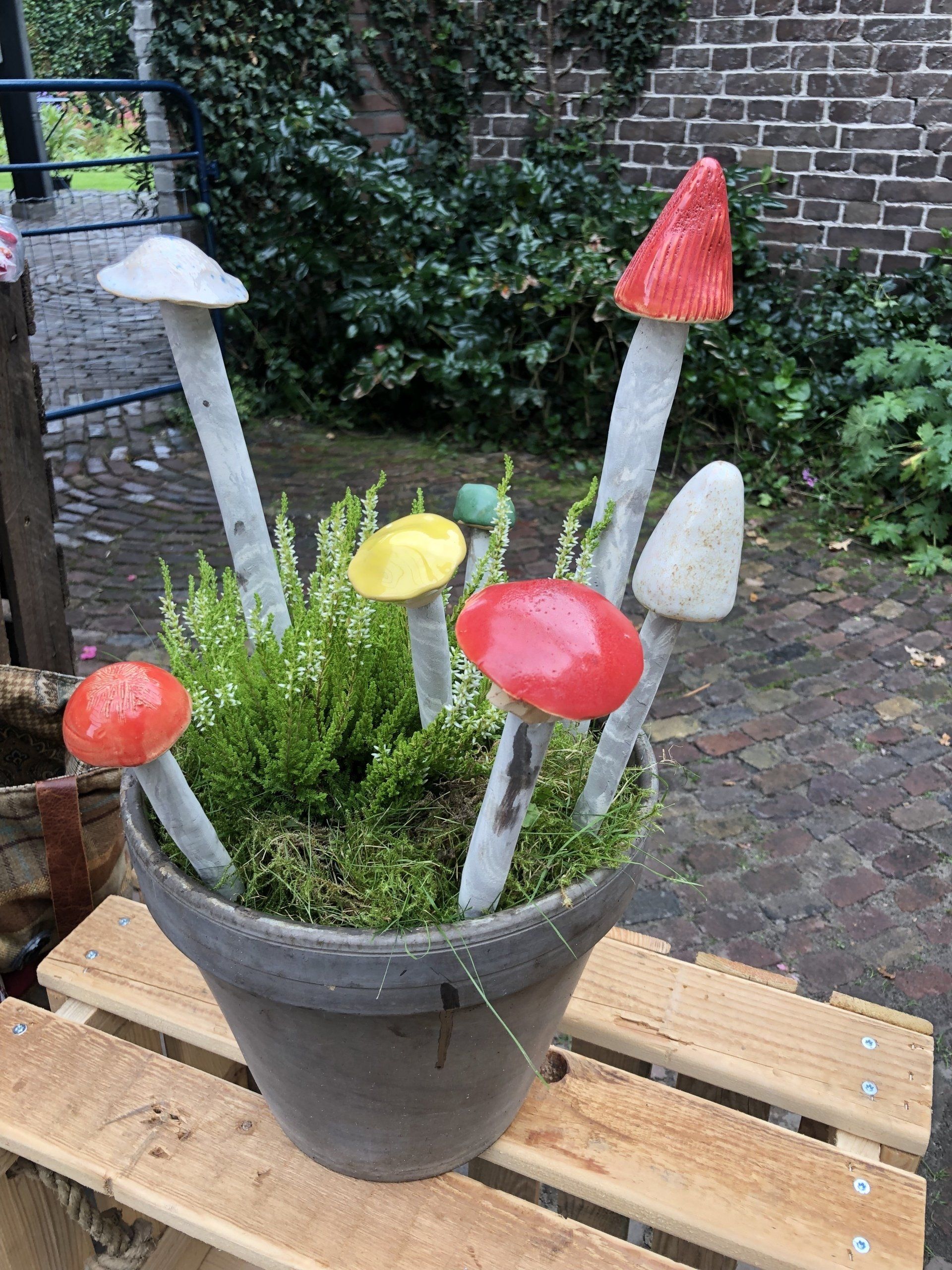 Een pot met kleurrijke paddenstoelentuinkunst, geplaatst op een houten pallet buiten.