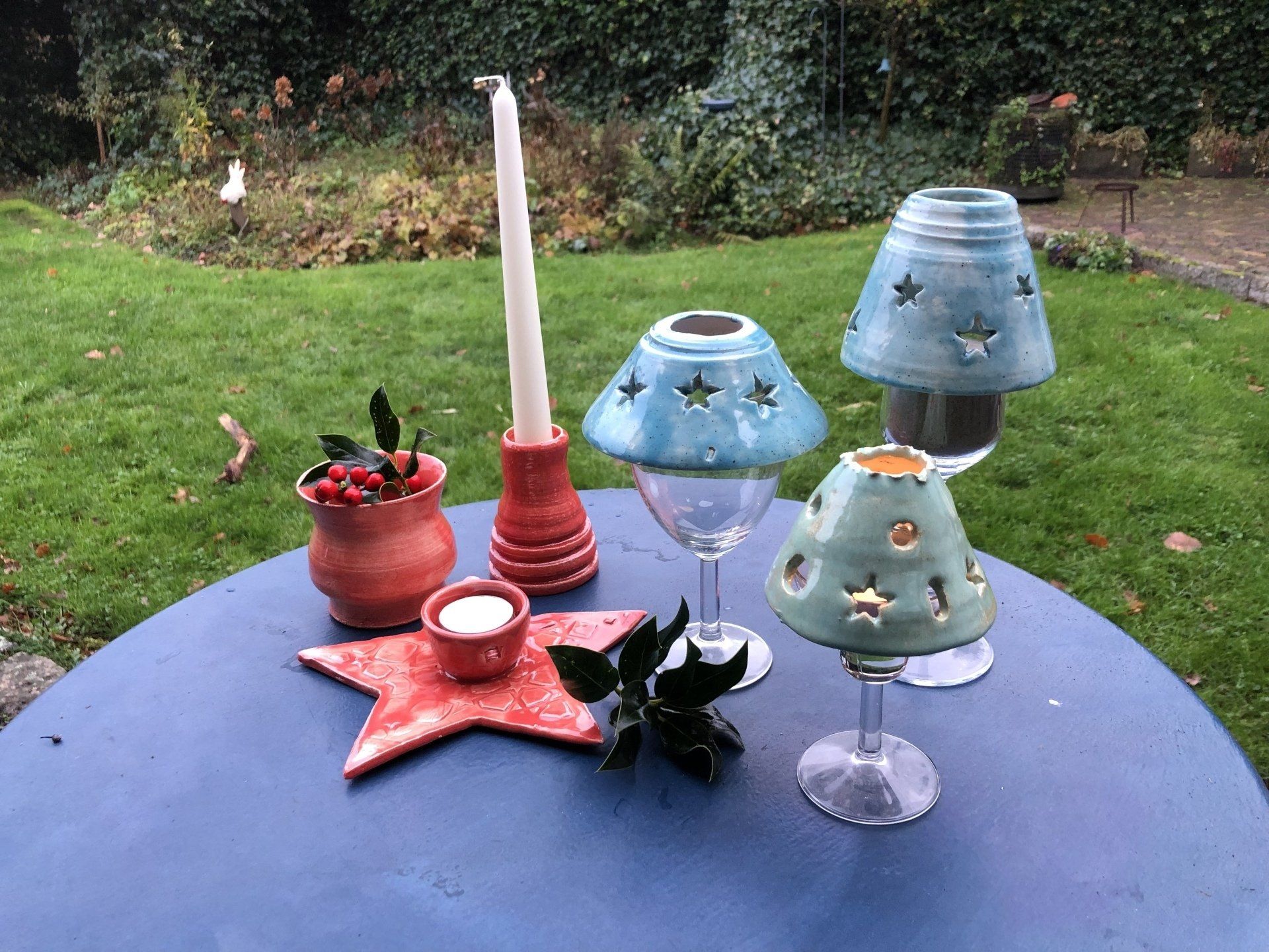 Een tafel met handgemaakte keramische kandelaars in diverse kleuren en vormen, geschikt voor buiten.