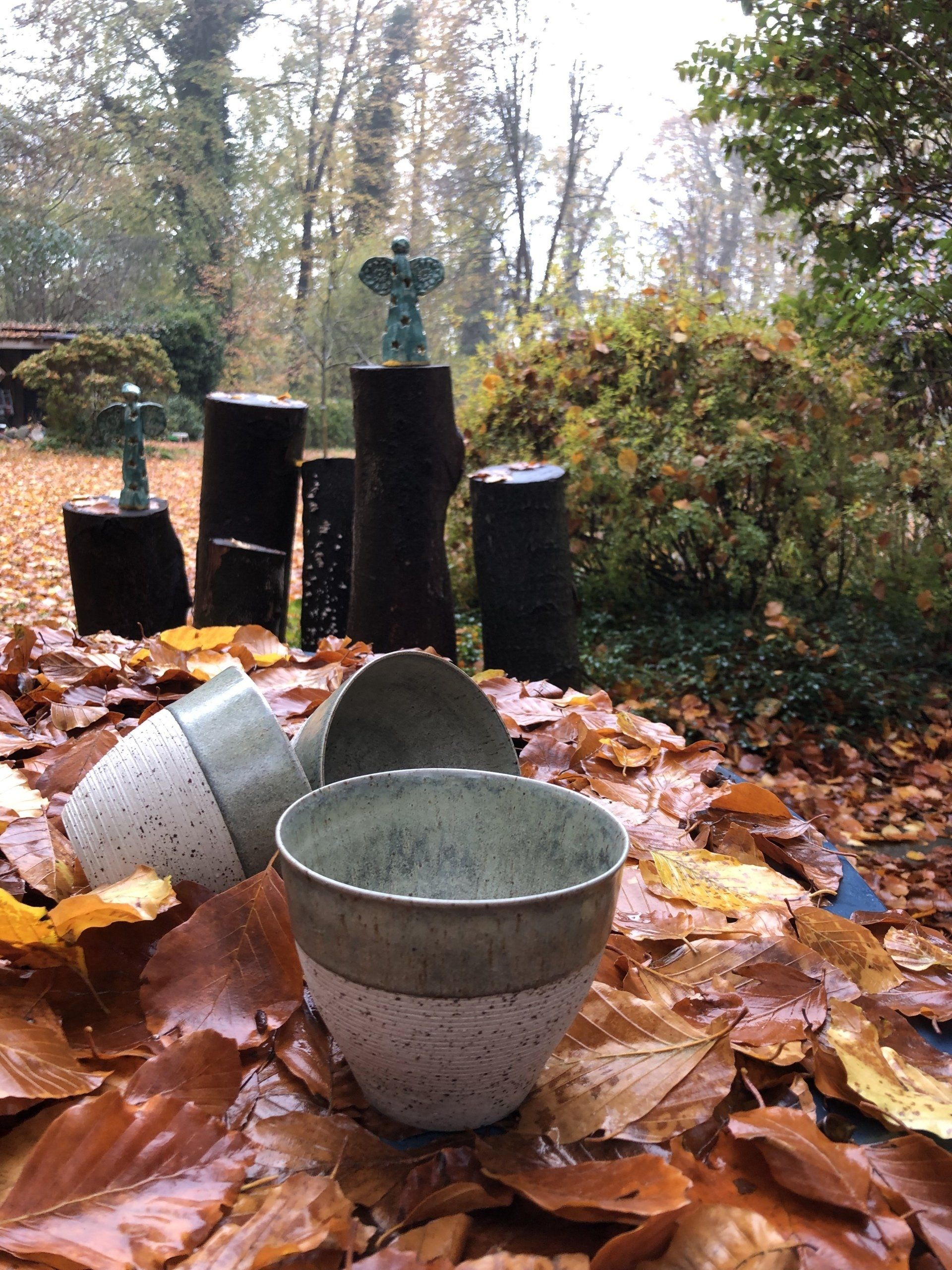 Keramische potten tussen herfstbladeren; kleine sculpturen op boomstronken op de achtergrond.