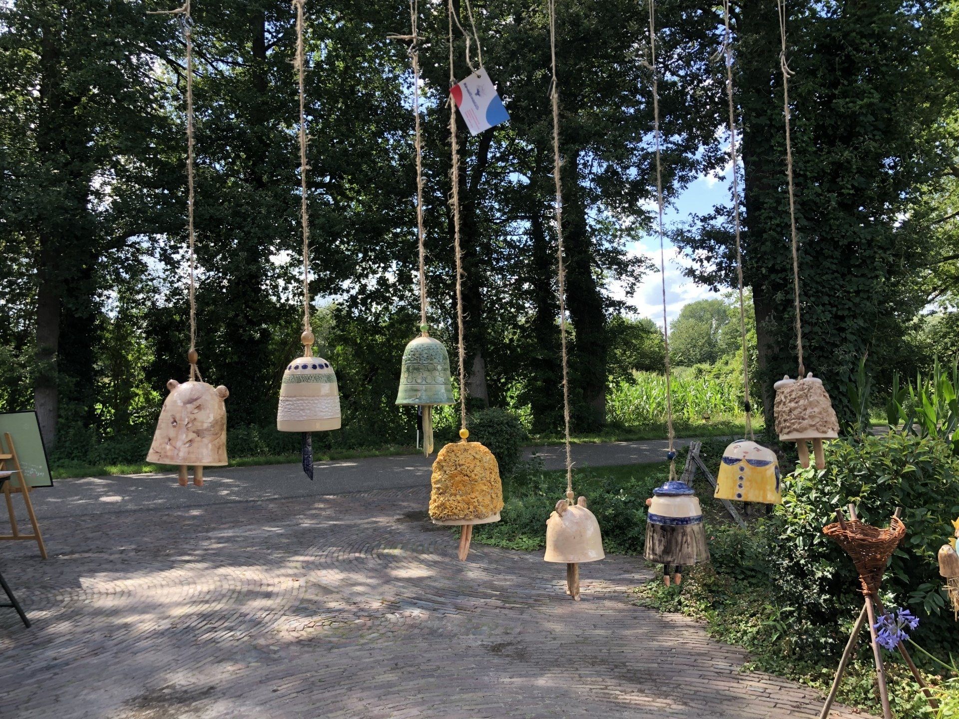Keramische bellen hangen aan touwen buiten, te midden van groen en bomen.