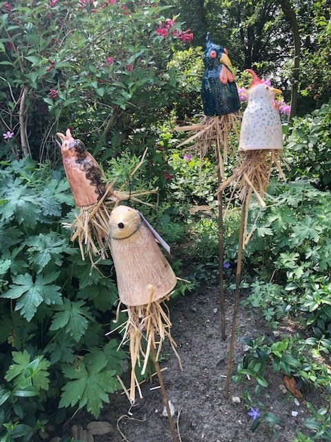 Speelse keramische vogelfiguurtjes op strolichamen, geplaatst in een weelderige groene tuin.