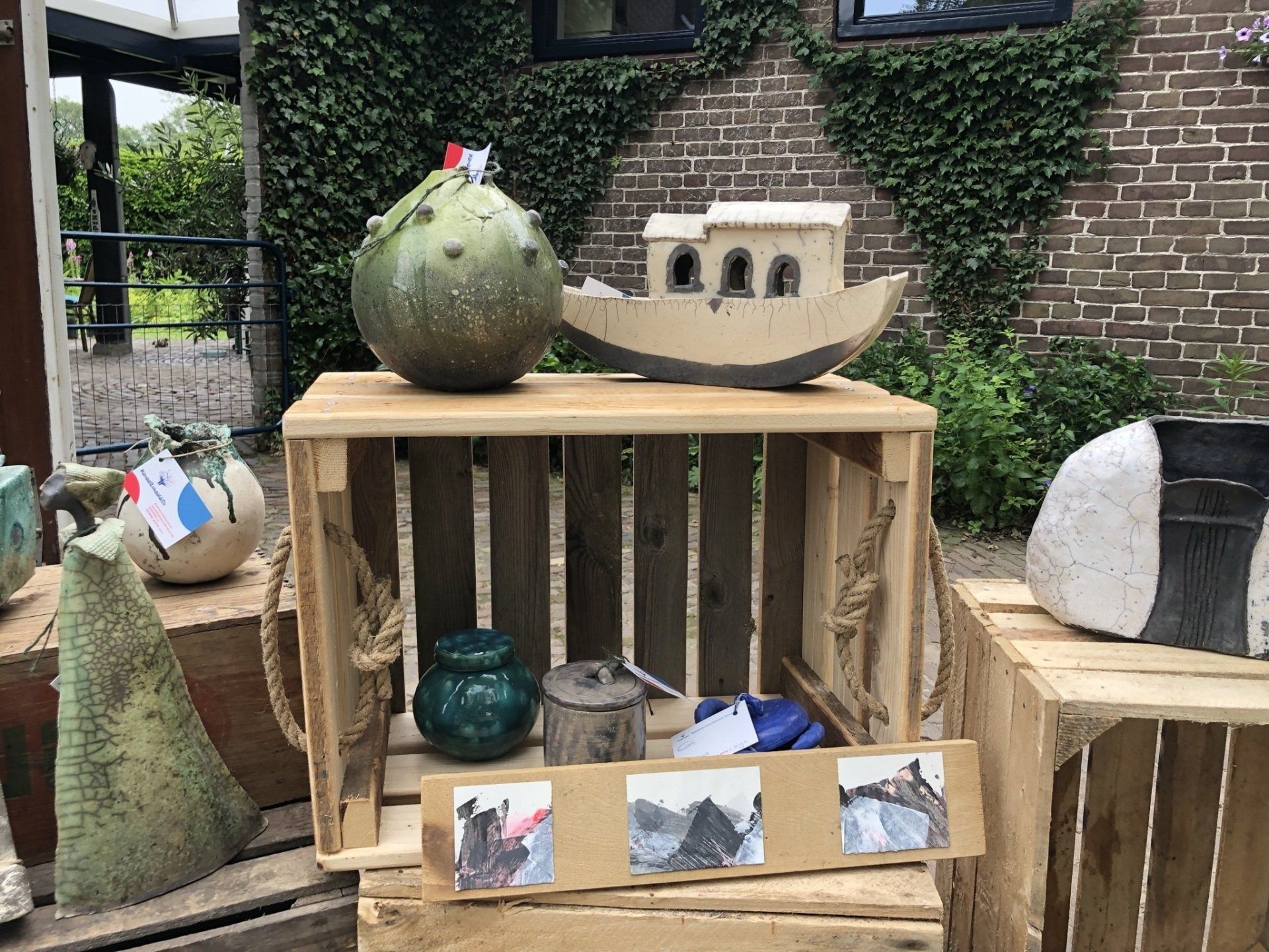 Keramische sculpturen tentoongesteld op houten kisten: een boot, een kalebasachtige vorm, vazen ​​en abstracte kunst.