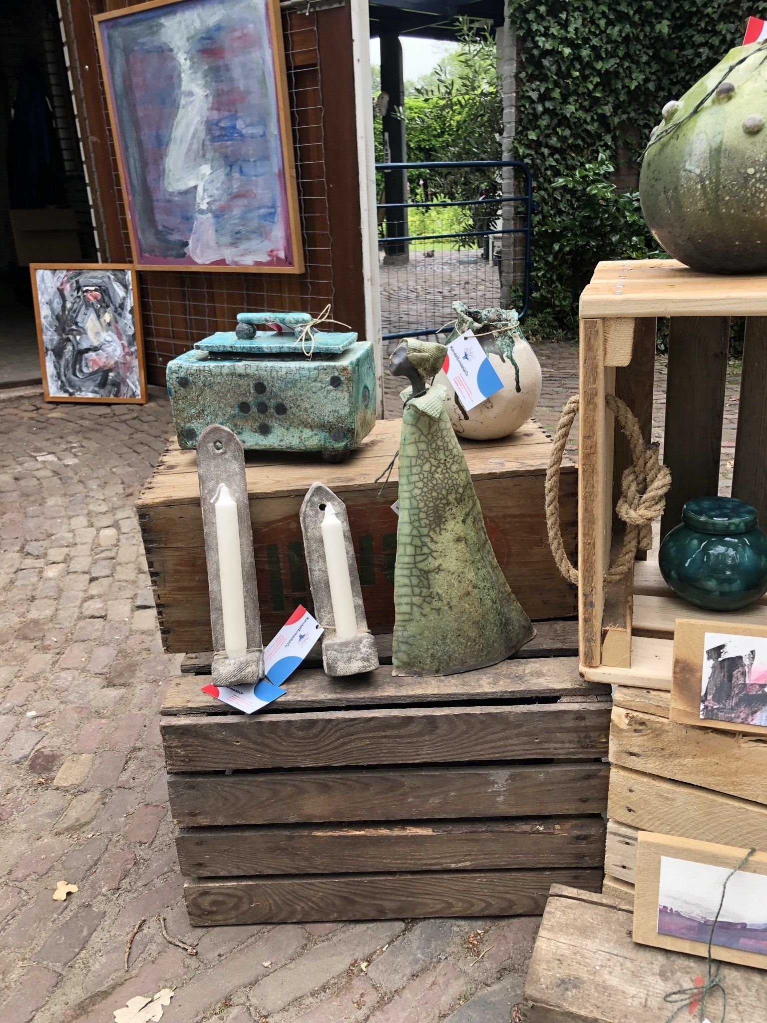 Buiten is keramische kunst te zien op houten kratten, met diverse vormen en kleuren.