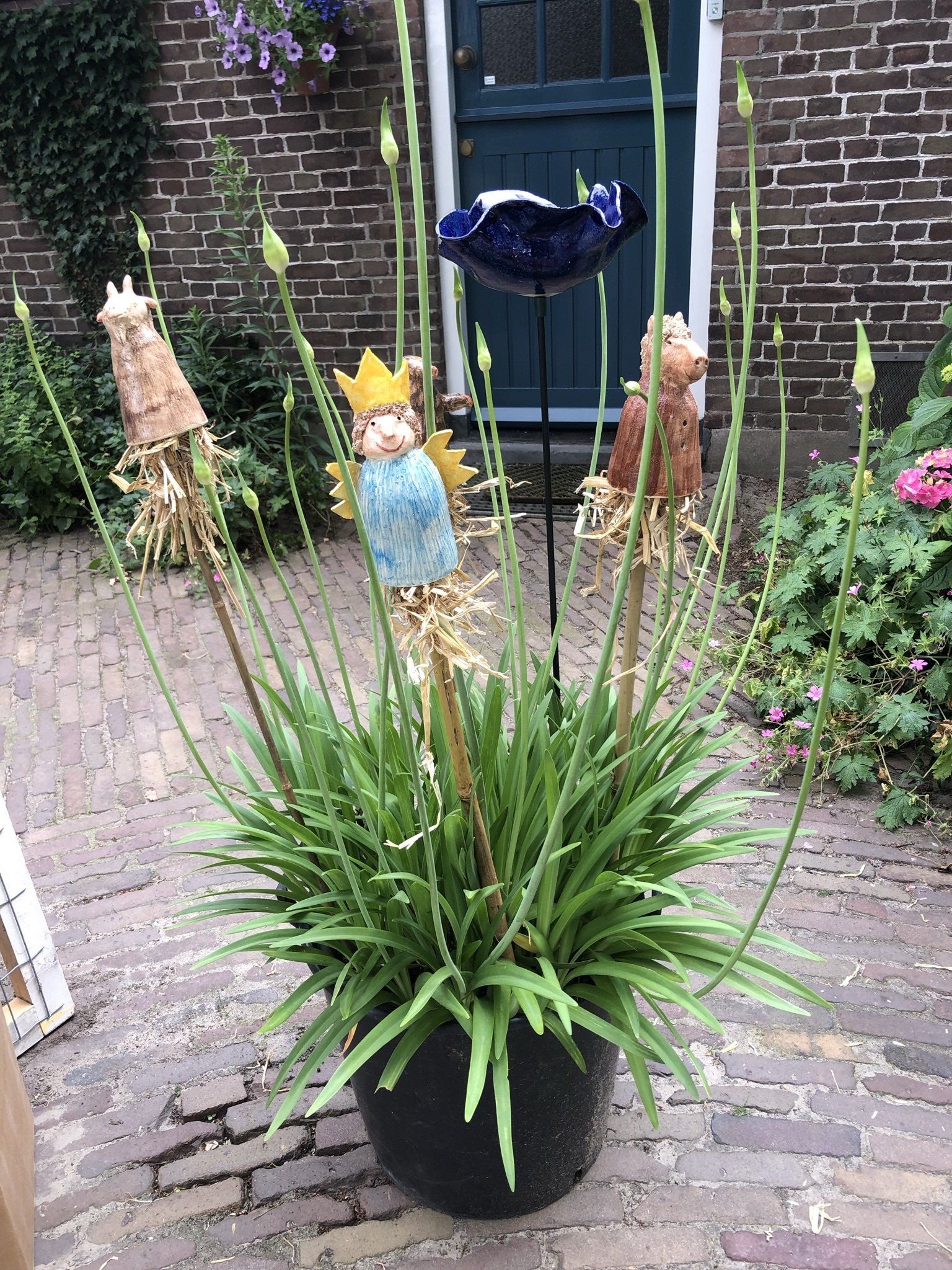 Een potplant met decoratieve beeldjes en een vogelbadje voor een bakstenen gebouw.