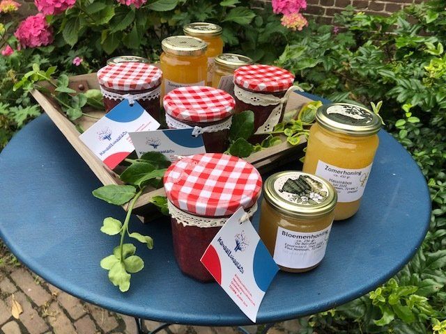 Potten jam en conserven met rode geruite deksels en kanten randjes staan uitgestald op een blauwe tafel buiten.