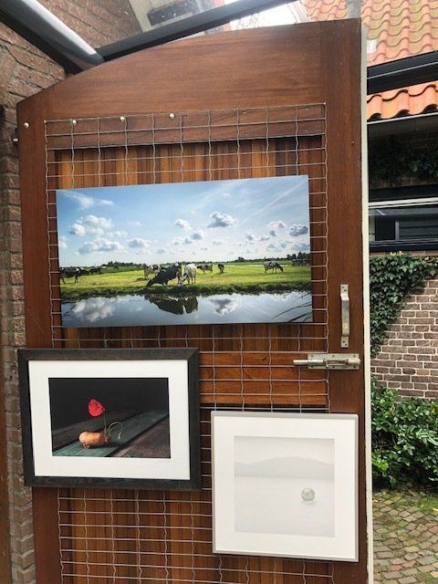 Kunstwerken, waaronder landschaps- en stillevenfoto's, zijn te zien op een houten deur.