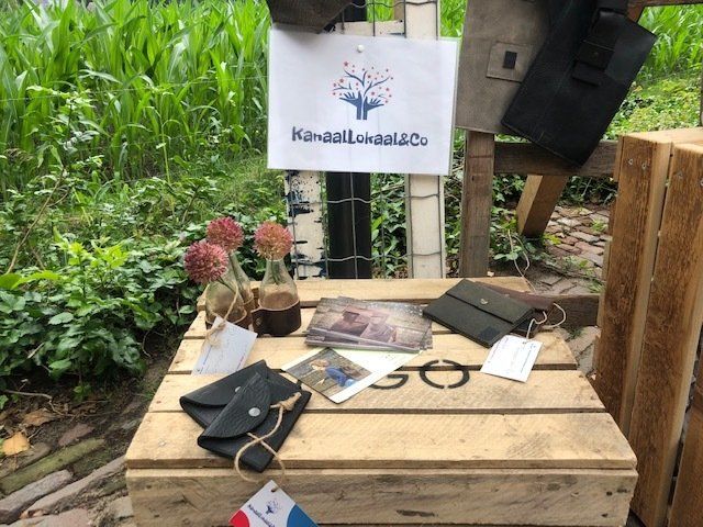 Een uitstalling van leren portemonnees, een bord met een logo en decoratieve elementen op een houten pallet in de buitenlucht.