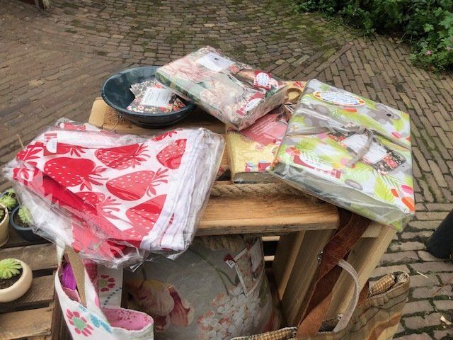 Een stapel verpakte textielproducten, waaronder artikelen met aardbeienprint, staat buiten op een houten display.