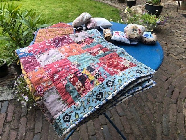Een patchworkdeken met kleurrijke bloemenstoffen op een blauwe tafel buiten.
