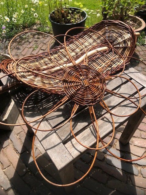 Een rieten mand in de vorm van een bloem, die buiten op een houten tafel staat.