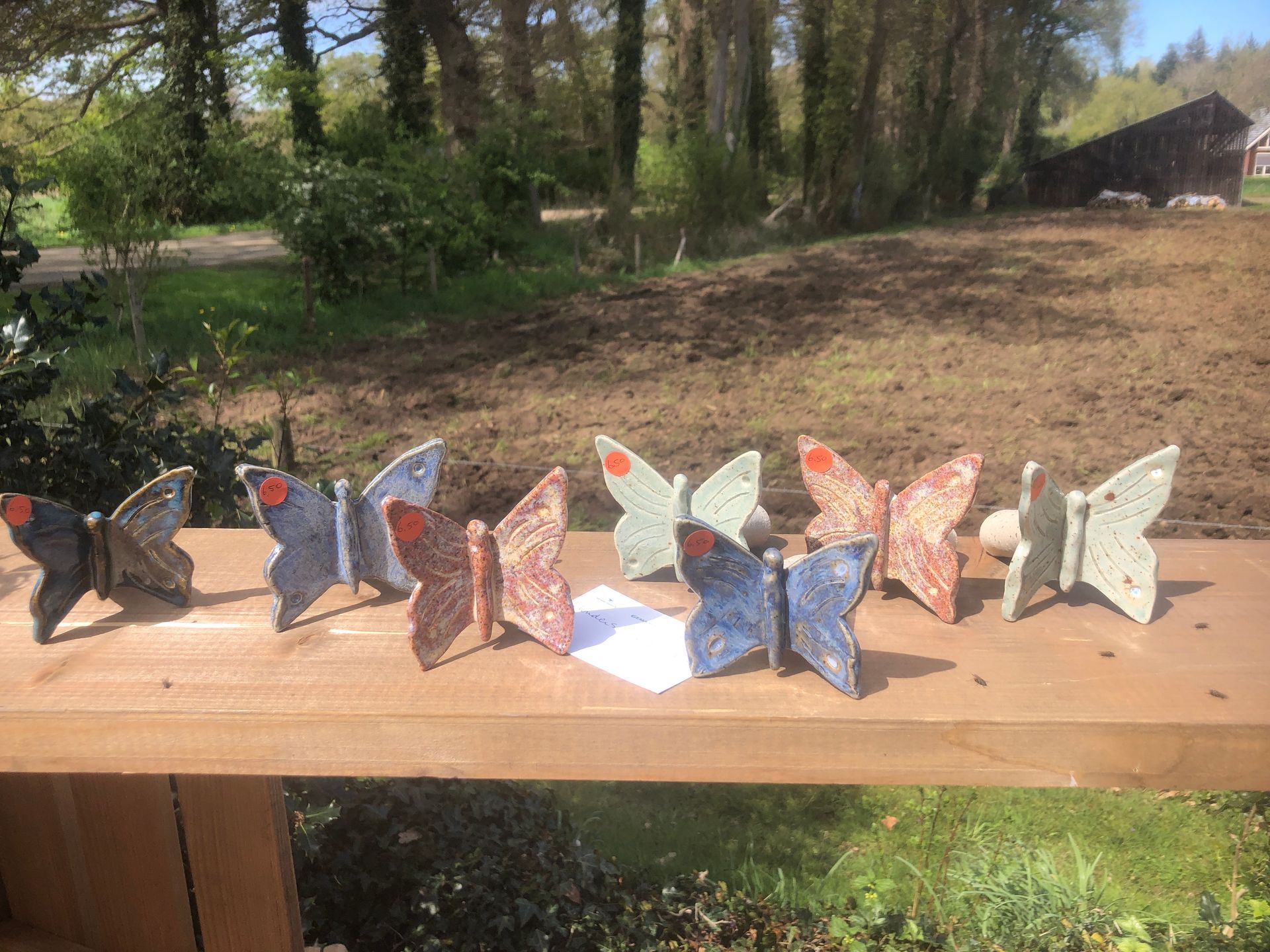 Een rij kleurrijke keramische vlinders staat op een houten ondergrond, buiten in een tuin.