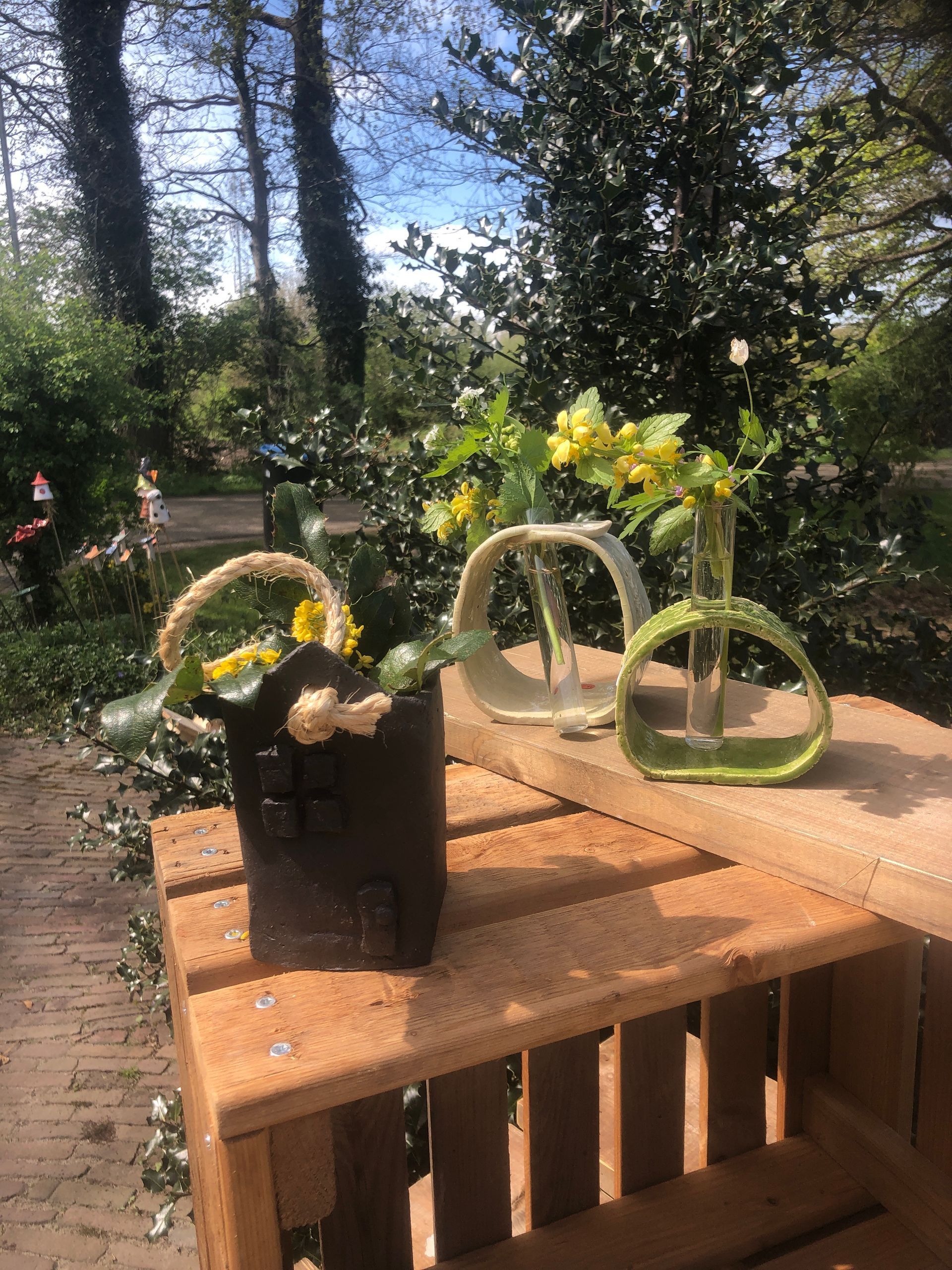 Houten krat met drie vazen en een mand met gele bloemen, buiten.