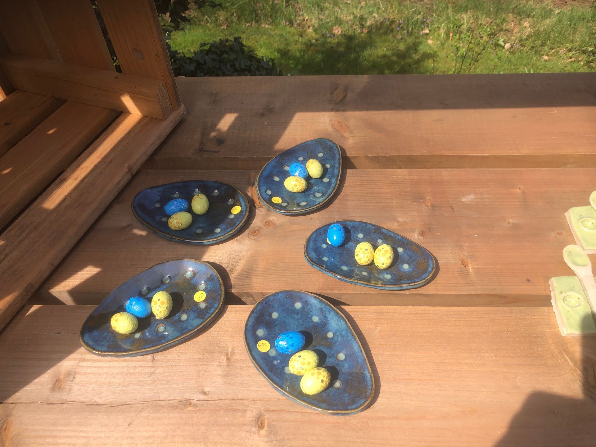Vijf eivormige keramische schaaltjes op een houten ondergrond, elk gevuld met blauwe en gele snoepjes.