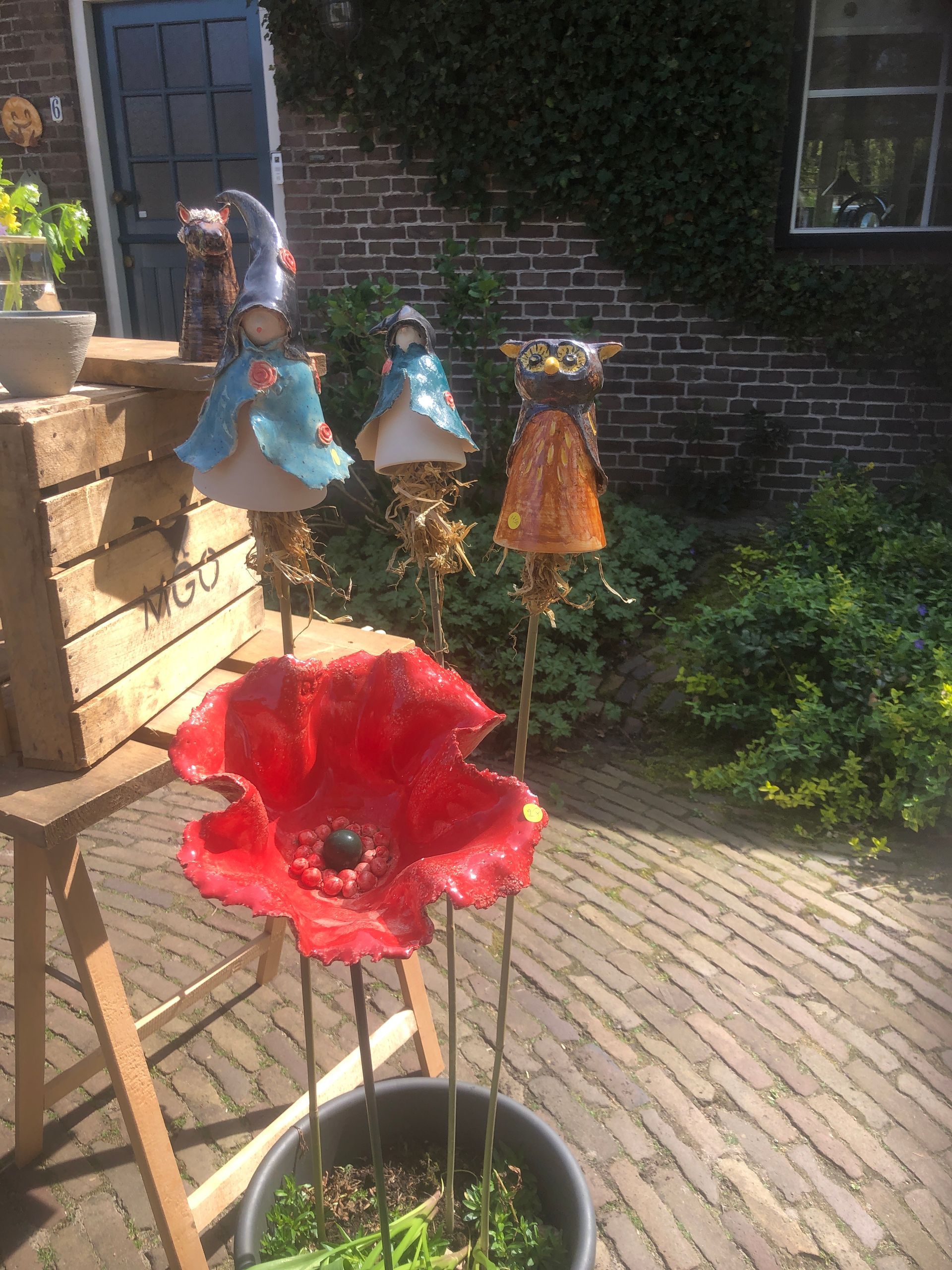 Tuinkunsttentoonstelling: rode bloem, speelse metalen sculpturen, achtergrond van bakstenen muur.