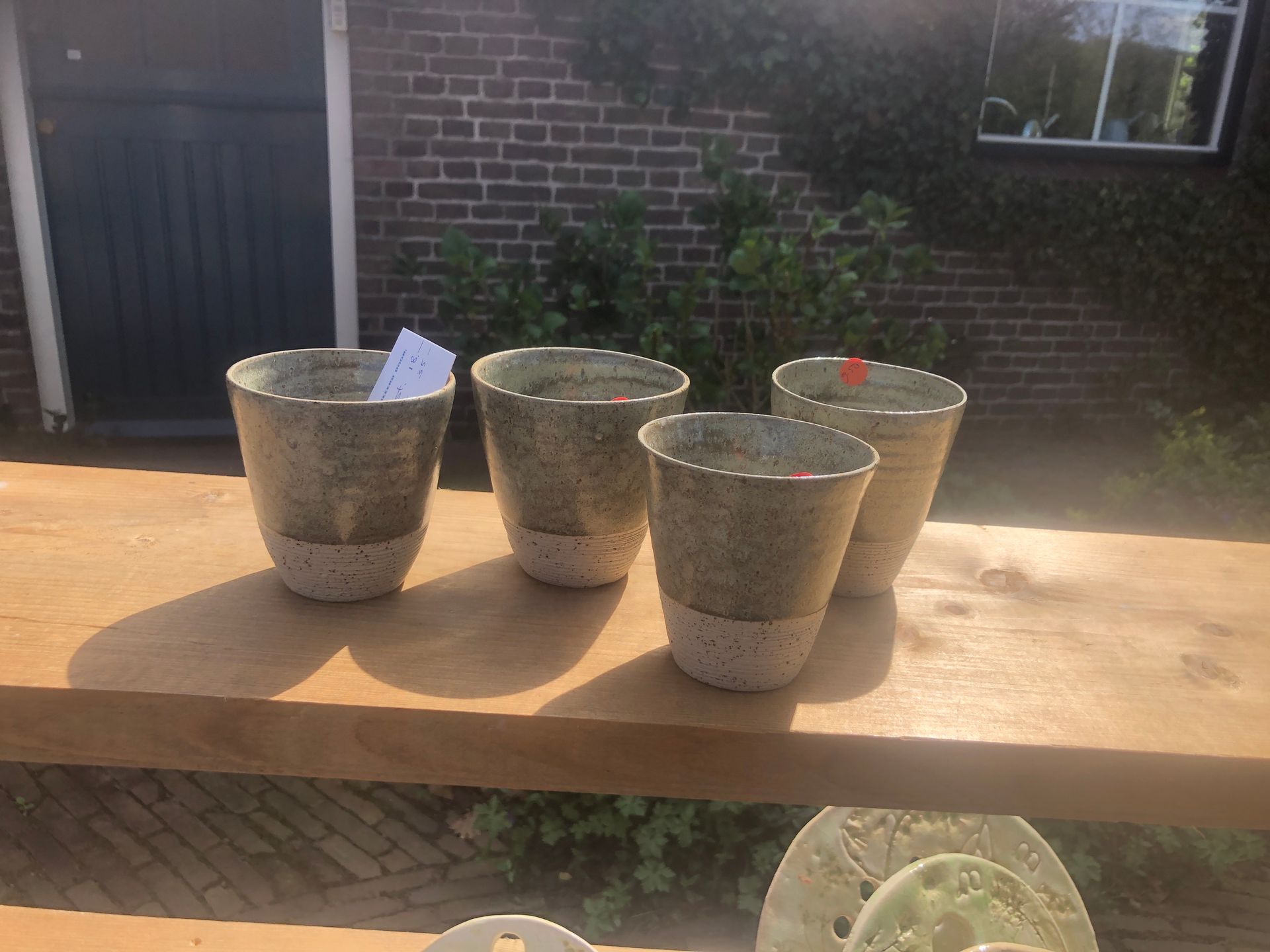 Vier gespikkelde keramische plantenpotten op een houten tafel, voor een bakstenen gebouw en groen.