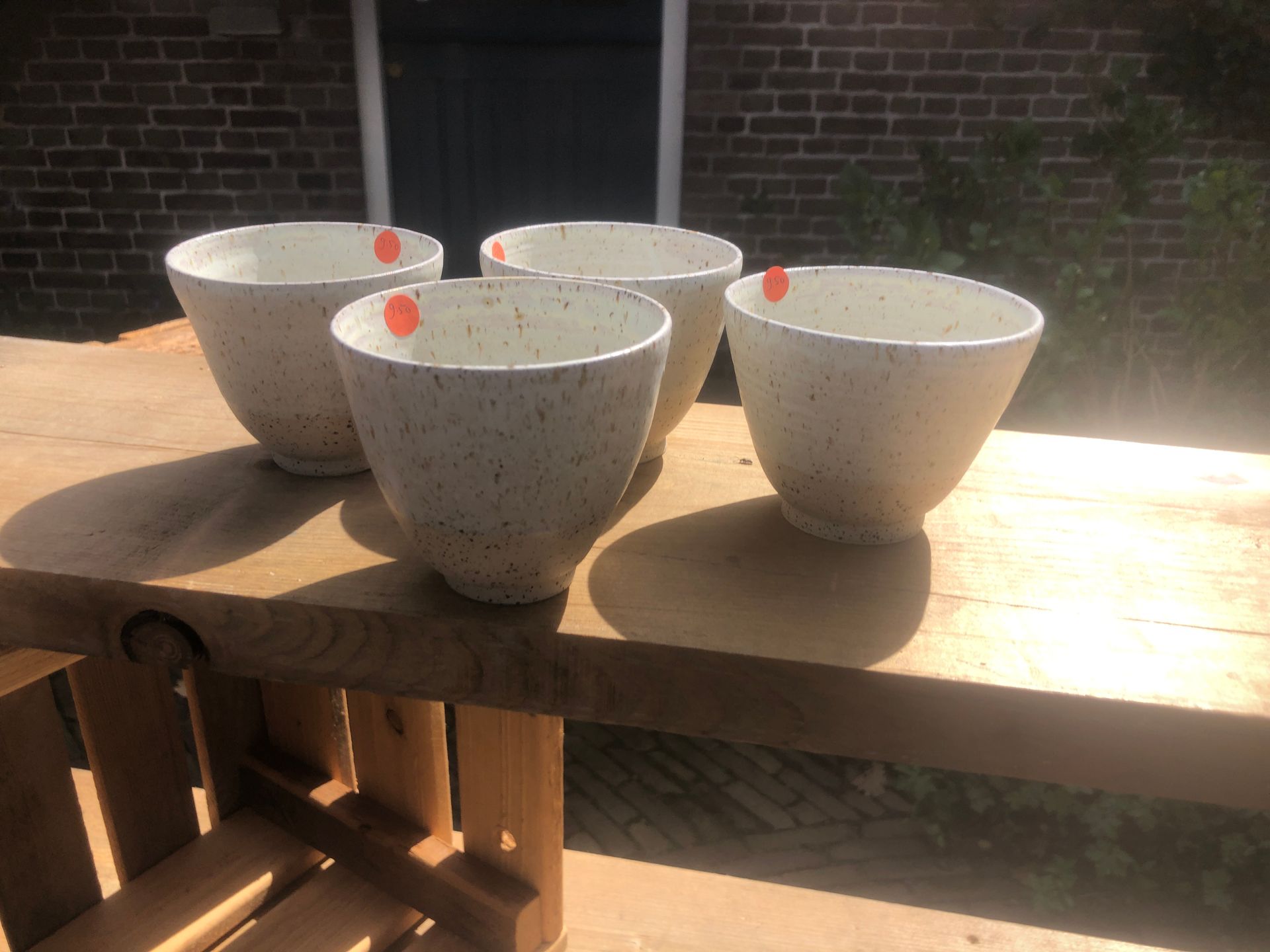 Vier gespikkelde witte keramische kommen op een houten tafel. Op elke kom zit een oranje prijssticker.