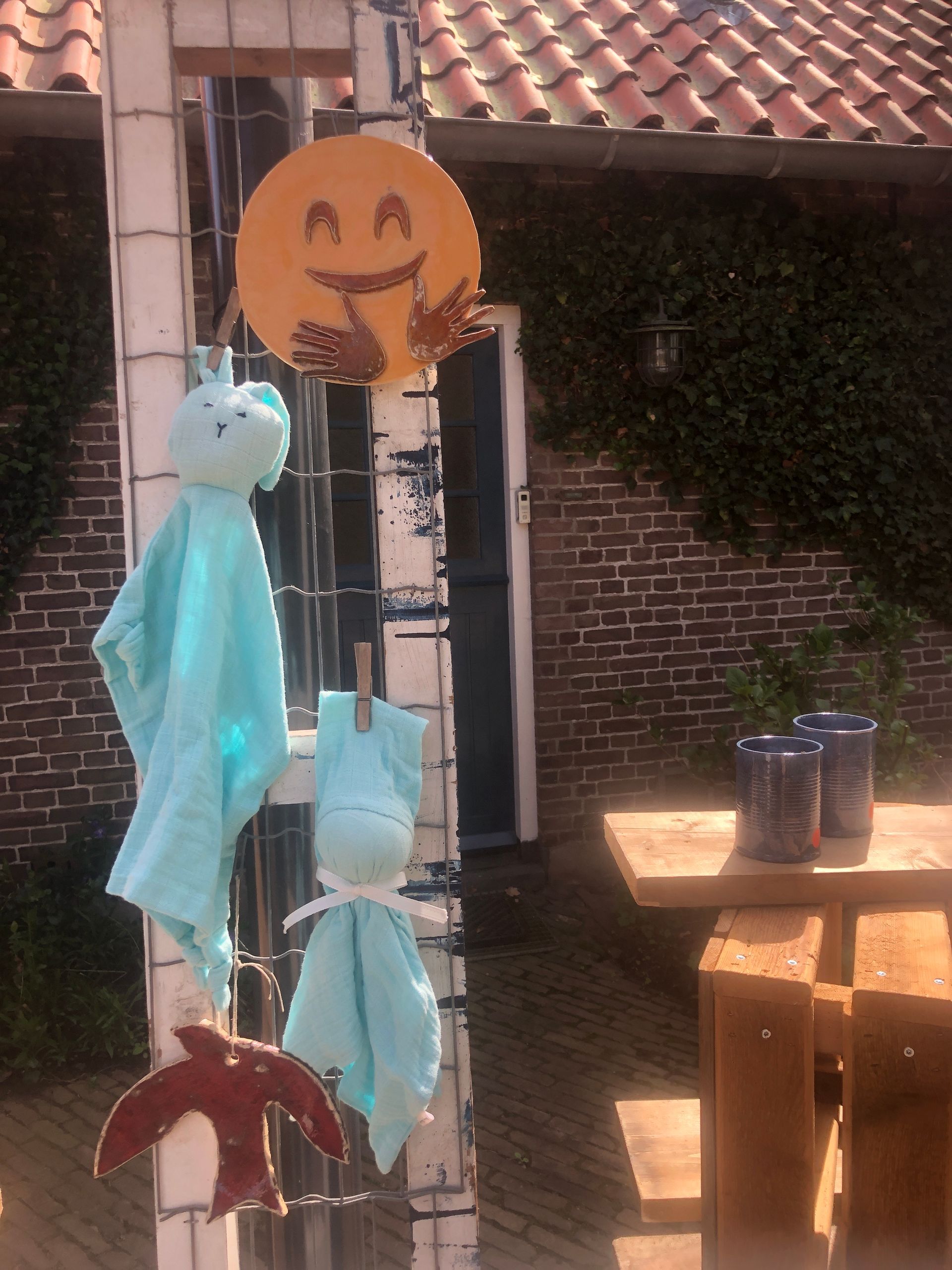 Decoraties hangen aan een witte paal op een steenhouwerij: een pompoengezicht, blauwe stoffen spookjes en een vogel.