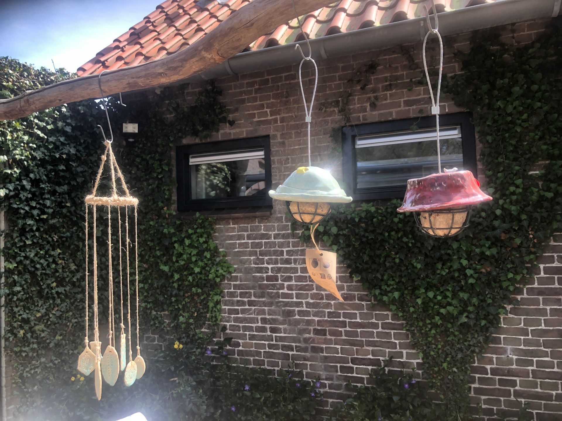 Windgong en hangende vogelvoederhuisjes buiten een met klimop begroeid bakstenen gebouw.