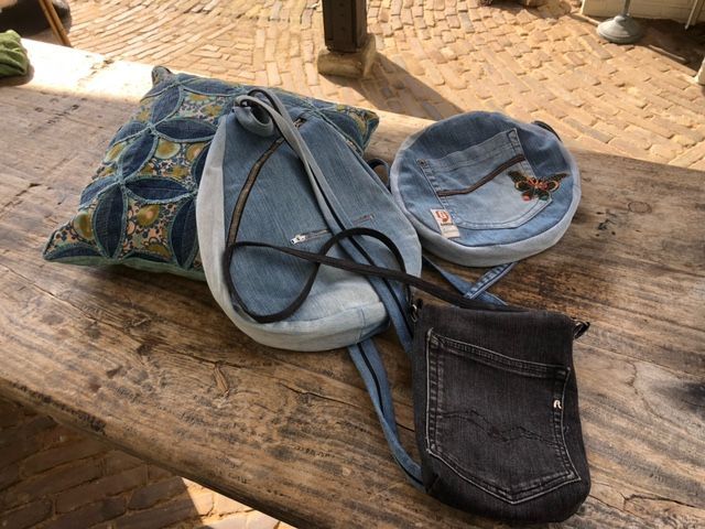 Een assortiment denim tassen en een decoratief kussen op een verweerde houten ondergrond.