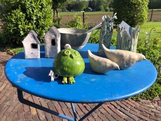 Blauwe tafel met keramische uil, vogels, huisjes en schalen in een tuinsetting.