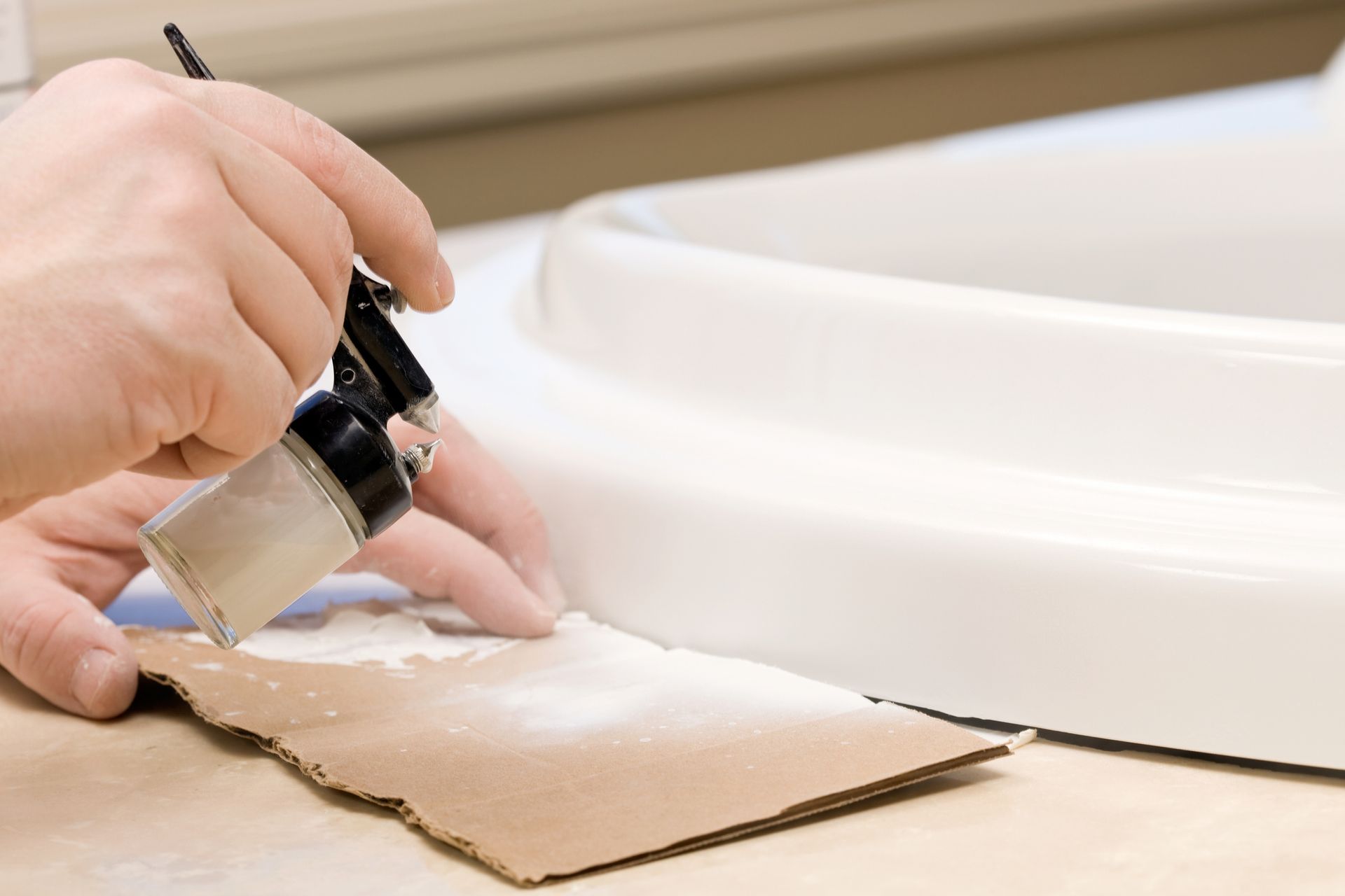 Hand applying adhesive to cardboard beside a white plastic bucket lid.