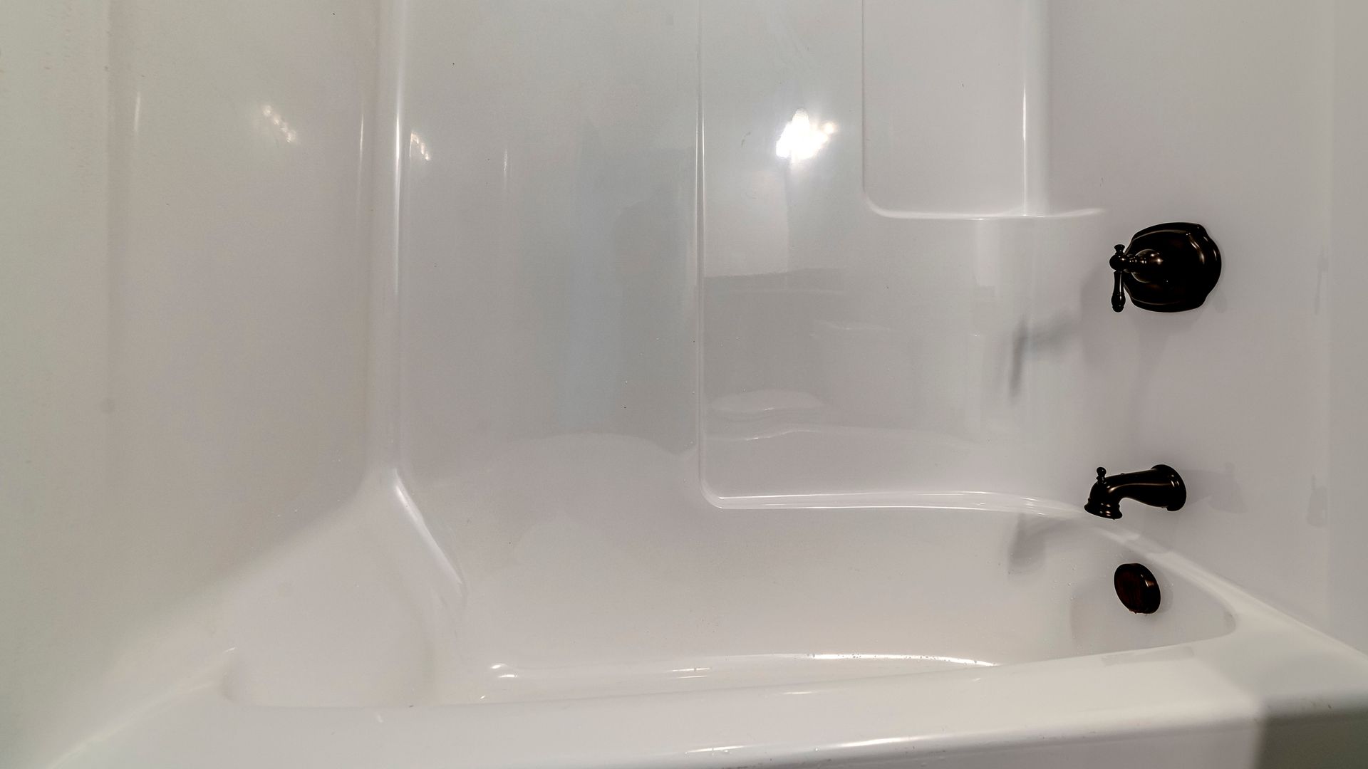 Technician reglazing bathtub with professional refinishing equipment in bathroom.