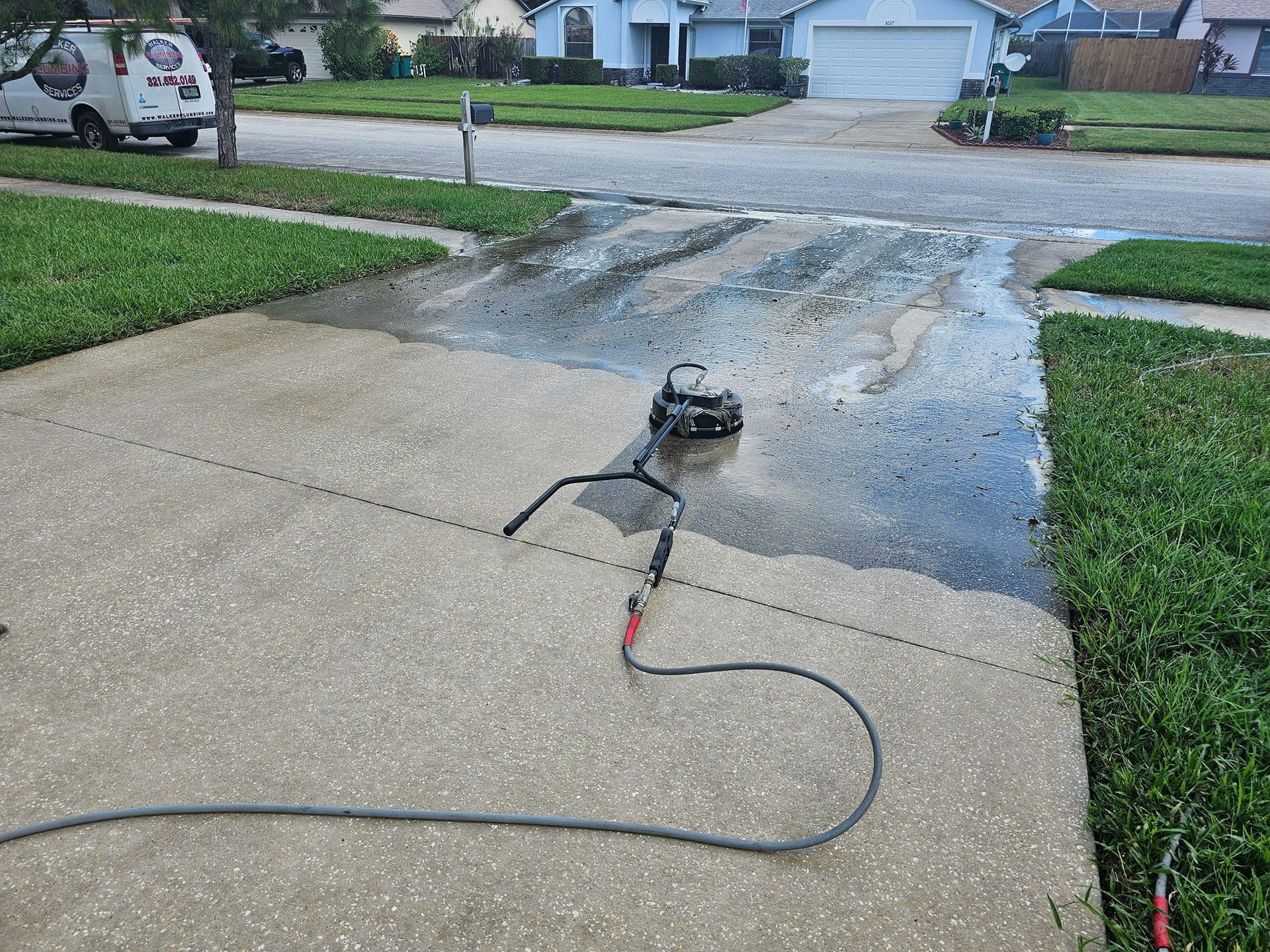 Pressure washer cleaning a concrete driveway in a suburban neighborhood.