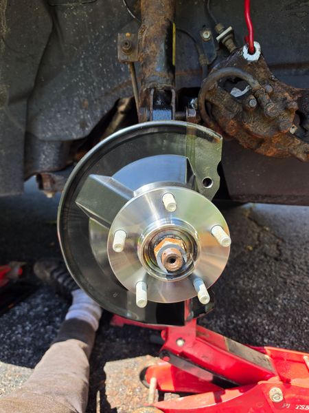 Car wheel hub and brake rotor exposed in wheel well, with red jack underneath.