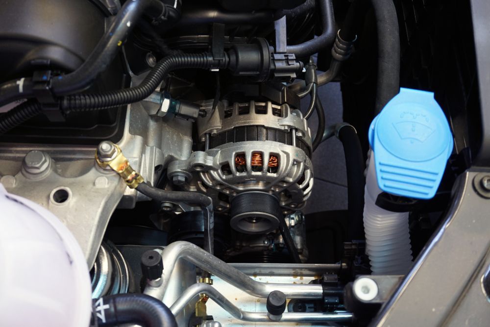 Car engine bay with alternator, hoses, and a blue fluid cap on the right